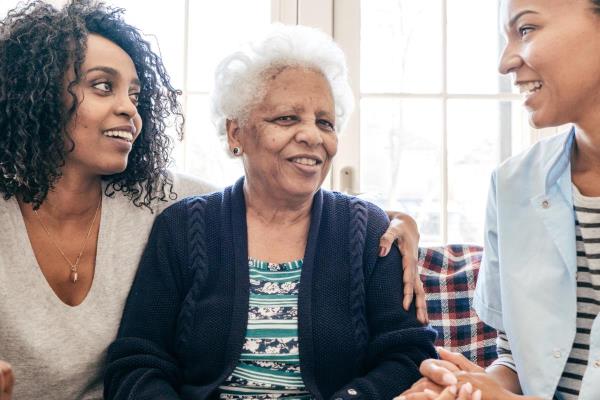 A caregiver talks with a client and her daughter, representing the type of communication that is vital when taking on a person-centered care approach.