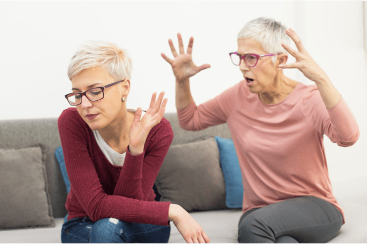 Two women sitting on a couch one yelling at the others back 1 