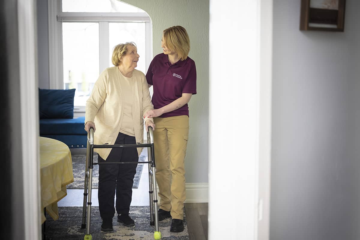 Home Instead Care Professional helping an Arthritis Care Senior get around the house with her walker 1 