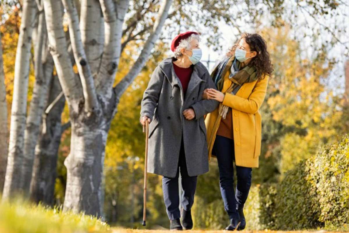 Masked senior and caregiver walking in the park