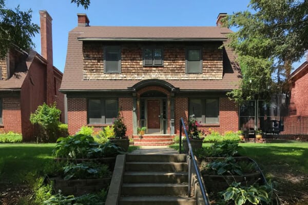 A charming two-story historic brick home with a well-maintained garden and welcoming front steps, emphasizing the comfort of familiar surroundings.